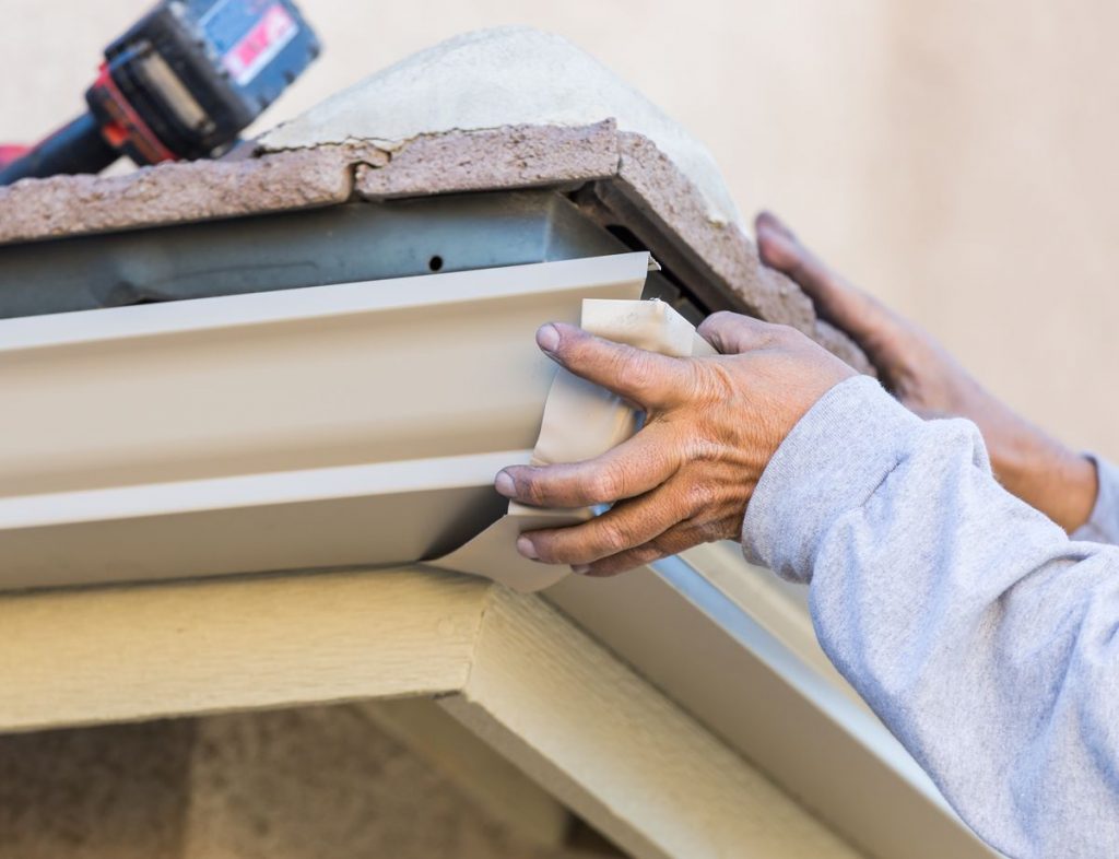 Worker Attaching Aluminum Rain Gutter to Fascia of House.