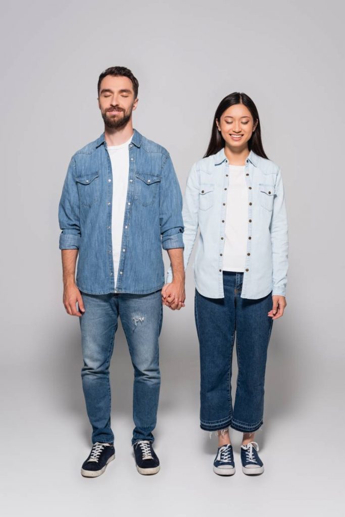 full length view of interracial couple in denim clothes and gumshoes holding hands while standing